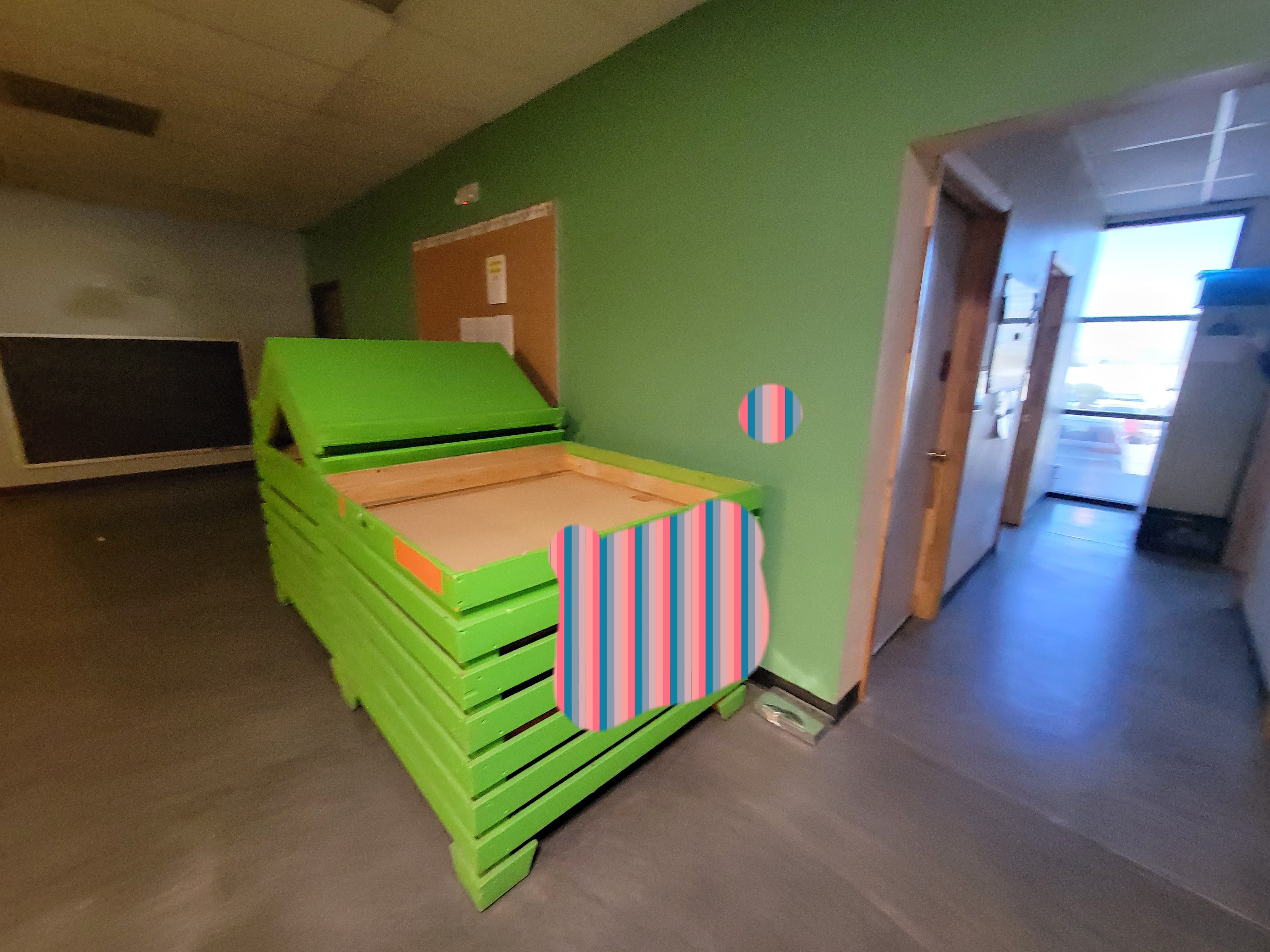 Green storage unit that was used to display products lined to the wall with a board to the right, a hallway at the end and a chalk board behind it.